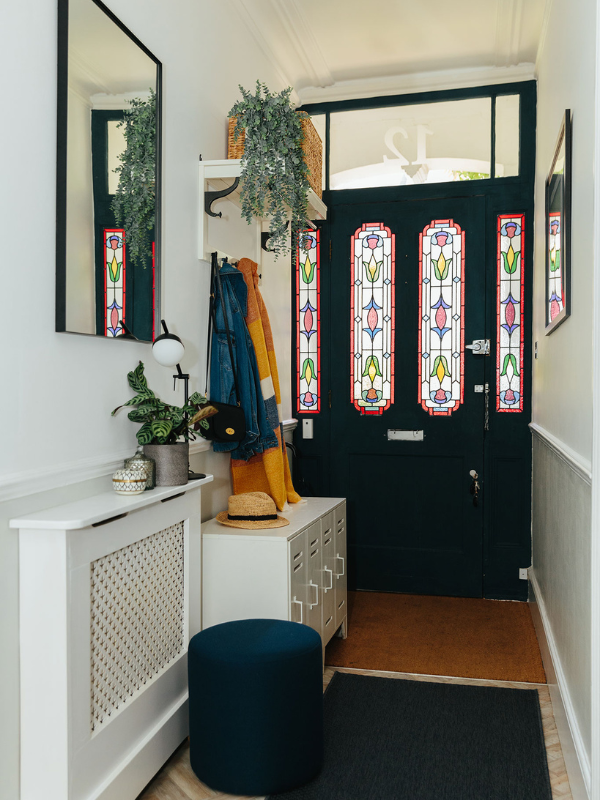 hallway with stain glass door and plants on white cabinets