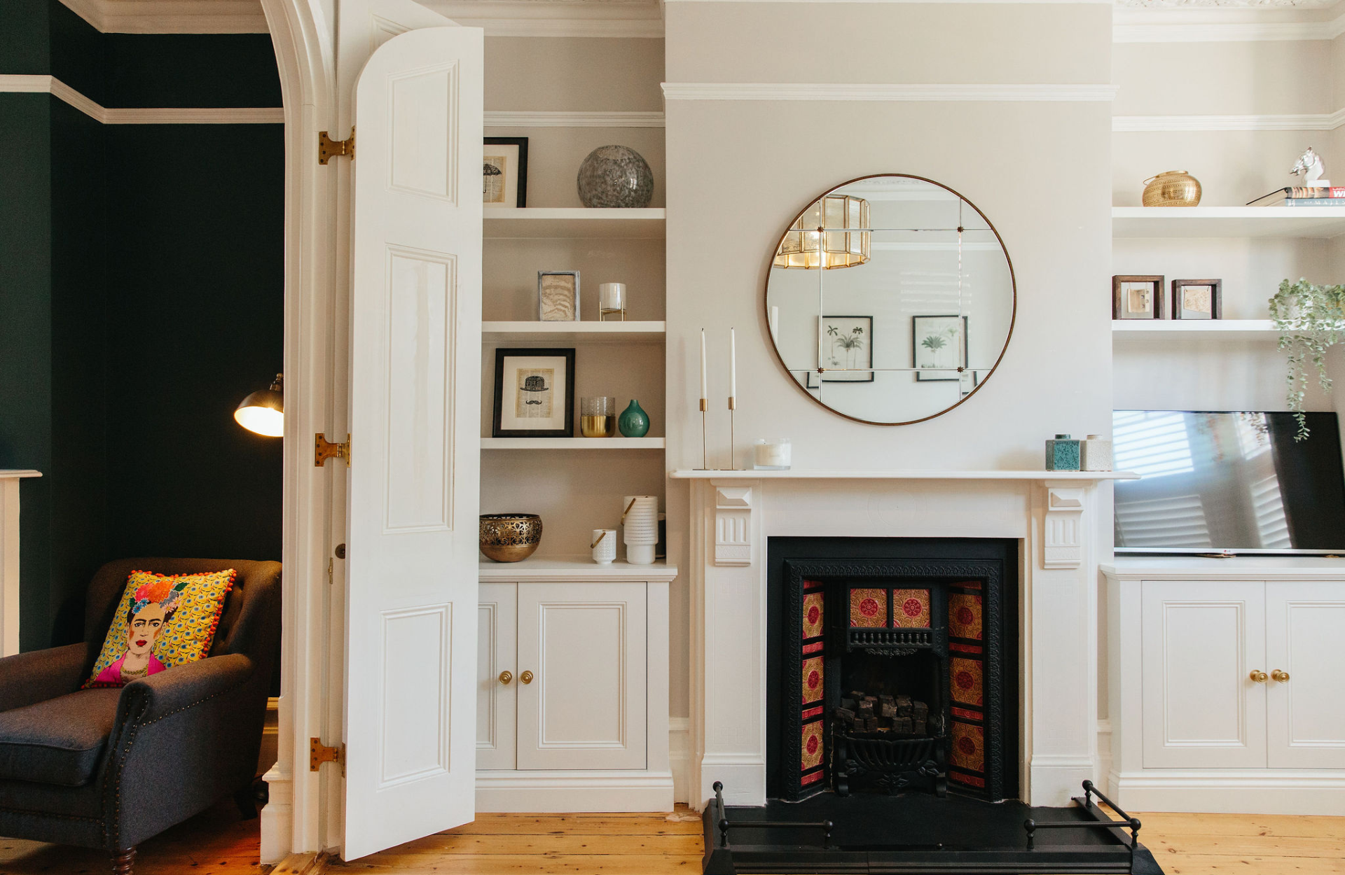 A wall with a chimney breast and round mirror above fire place