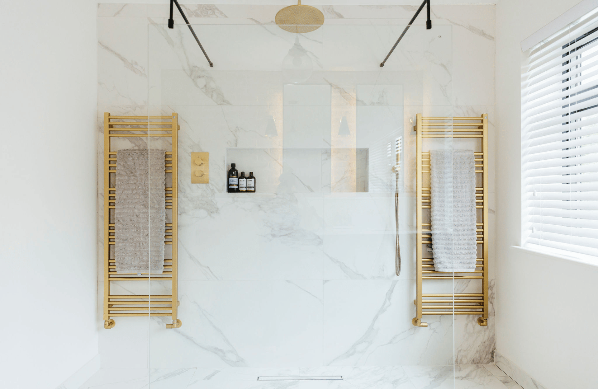 Large bathroom with white marble tiles and gold towel rails